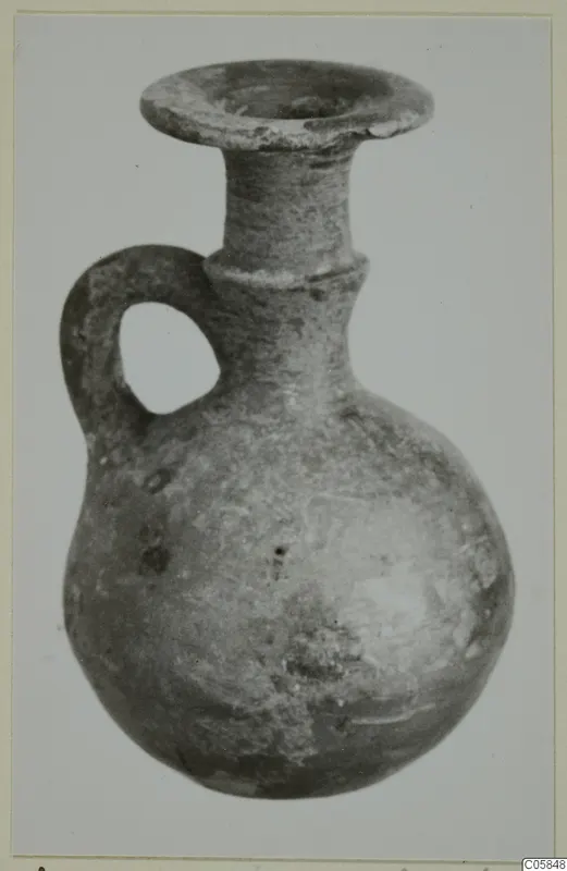 Grey polished ware jug with a round body, narrow neck, flared rim and loop handle
