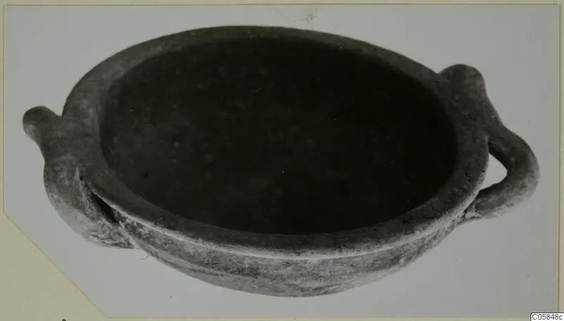 Shallow grey pottery bowl with two small handles on opposite sides, photographed on a pale backdrop.