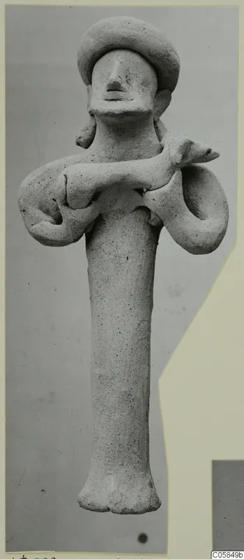 Terracotta statuette of a standing figure with a wide rounded headdress and arms bent outward, holding a small animal across its body.