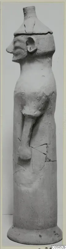 Terracotta figure with a cylindrical body, profile head and one bent arm, standing on a round base