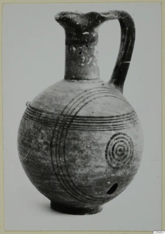 Round-bodied jug with a tall neck and loop handle, decorated with dark concentric circles and bands.