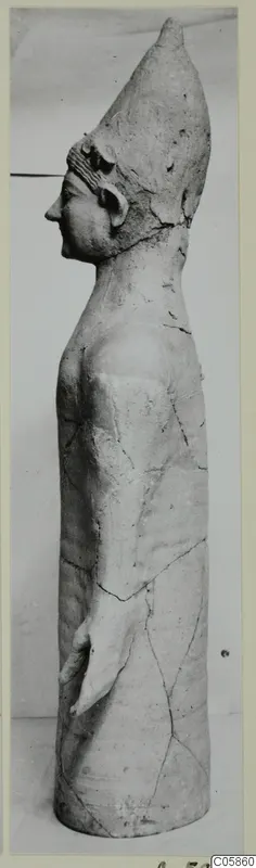 Terracotta standing figure from Mersinaki, shown in profile facing left, with a tall conical headdress.