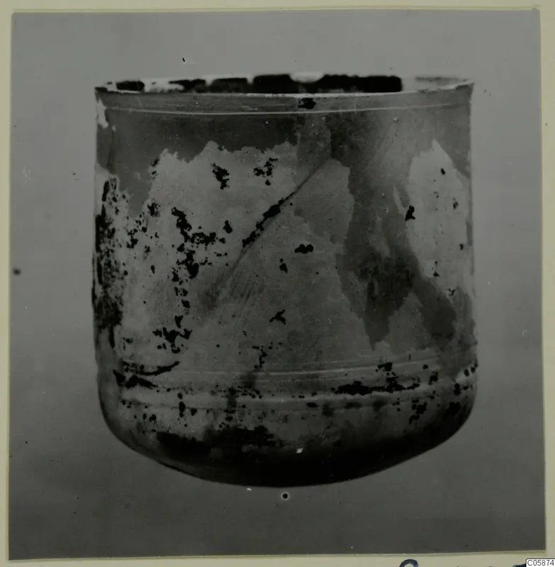 Blown glass vessel from Idalion, straight-sided with a rounded base, its surface pale and dark patched from weathering