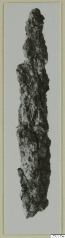 Corroded iron weapon, long and narrow, photographed against a pale background.