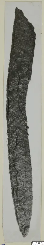 Corroded iron knife with a long, narrow, slightly curved blade, photographed upright