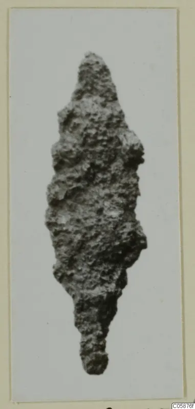 Corroded iron weapon with a pointed, leaf-shaped blade and a narrow tang, photographed on a card mount
