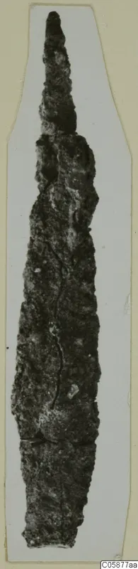 Corroded iron knife from Idalion with a long pointed blade, shown on a pale card.