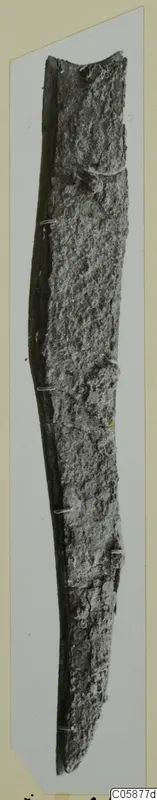 Long iron knife blade, heavily corroded, photographed upright against a pale mount.