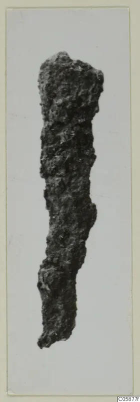 Iron Bronze Age knife, heavily corroded and crusted, photographed upright against a pale background.