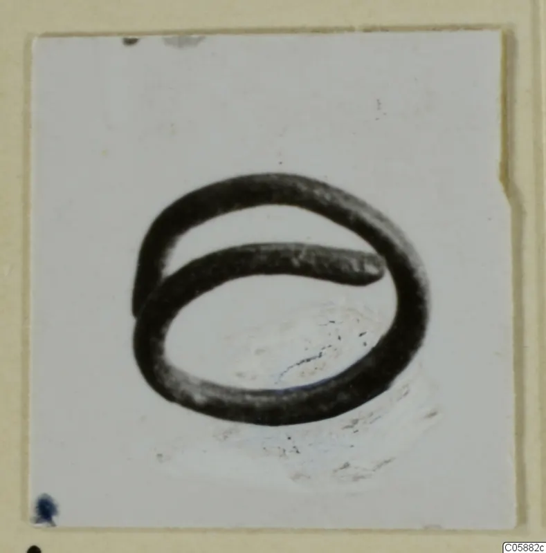 Bronze hair spiral, a dark wire coil of two overlapping loops, shown on a pale card.