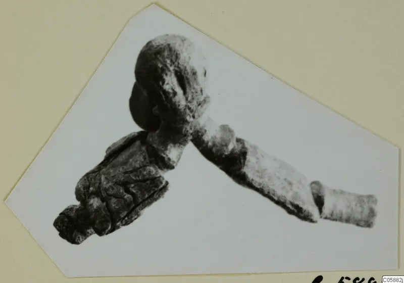 Bronze fibula photographed on a cut card mount, with a rounded head and a long bow extending diagonally
