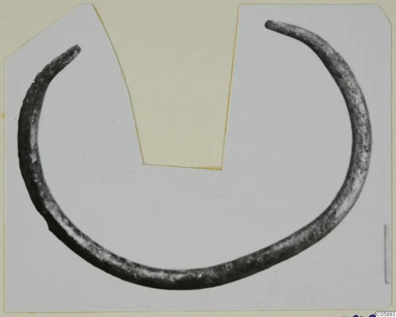 Open bronze bracelet with tapering ends, lying flat and photographed on a pale card mount.