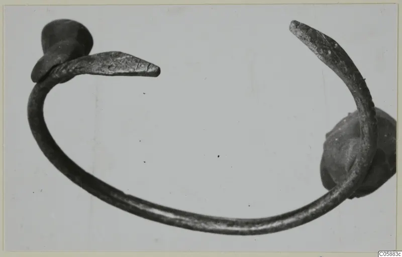 Bronze bracelet with an open ring and flattened, tapering terminals, photographed on a pale background.