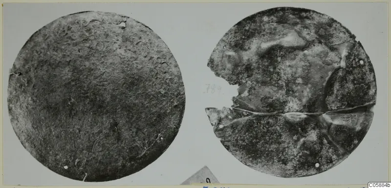 Two round bronze mountings side by side, one intact and one broken across its middle.