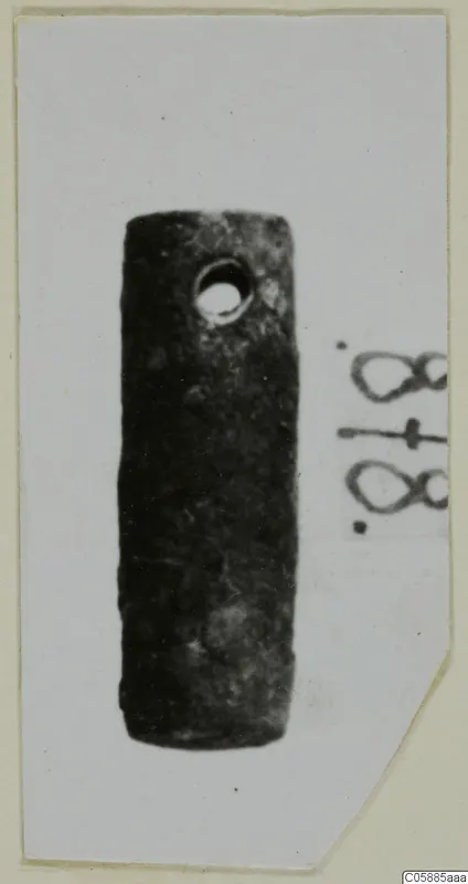 Cylindrical bronze fragment with a round hole near one end, photographed on a card