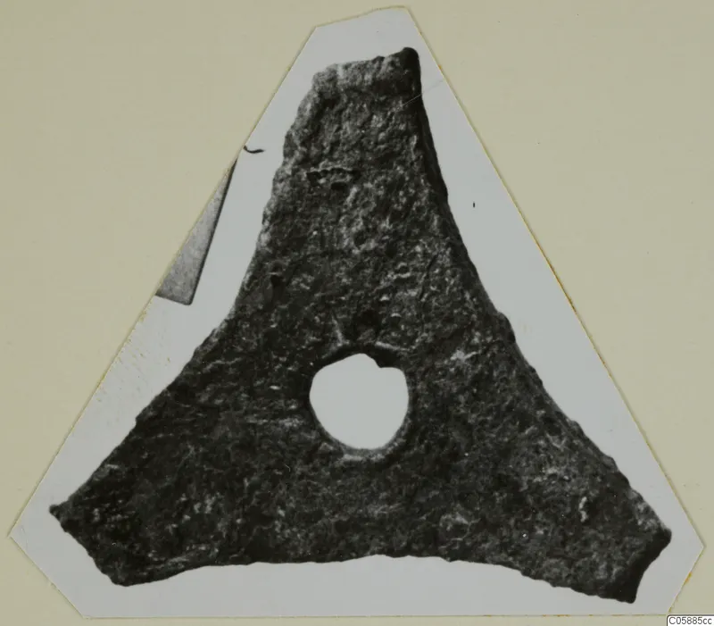 Triangular bronze fragment with a round hole near its centre, shown cut out and mounted on a card