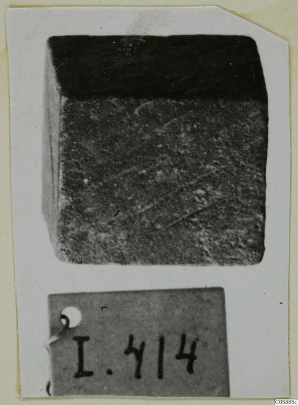 Cube-shaped bronze weight, dark and corroded, shown with its number label.