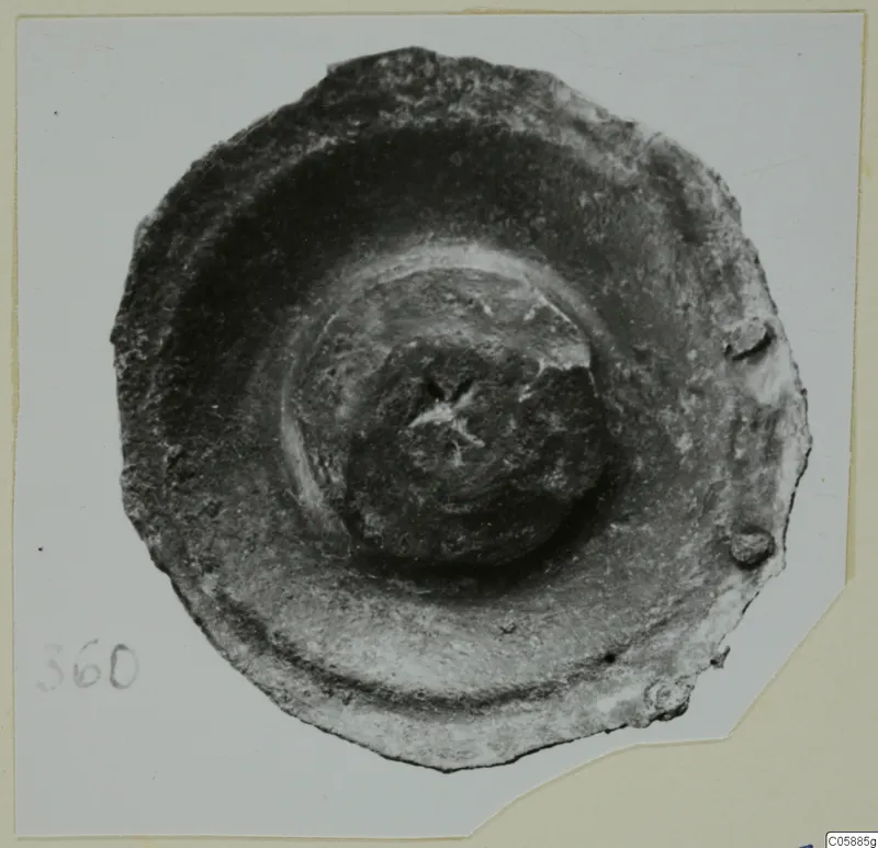 Corroded bronze disc-shaped mounting fragment with a central boss, photographed from above.