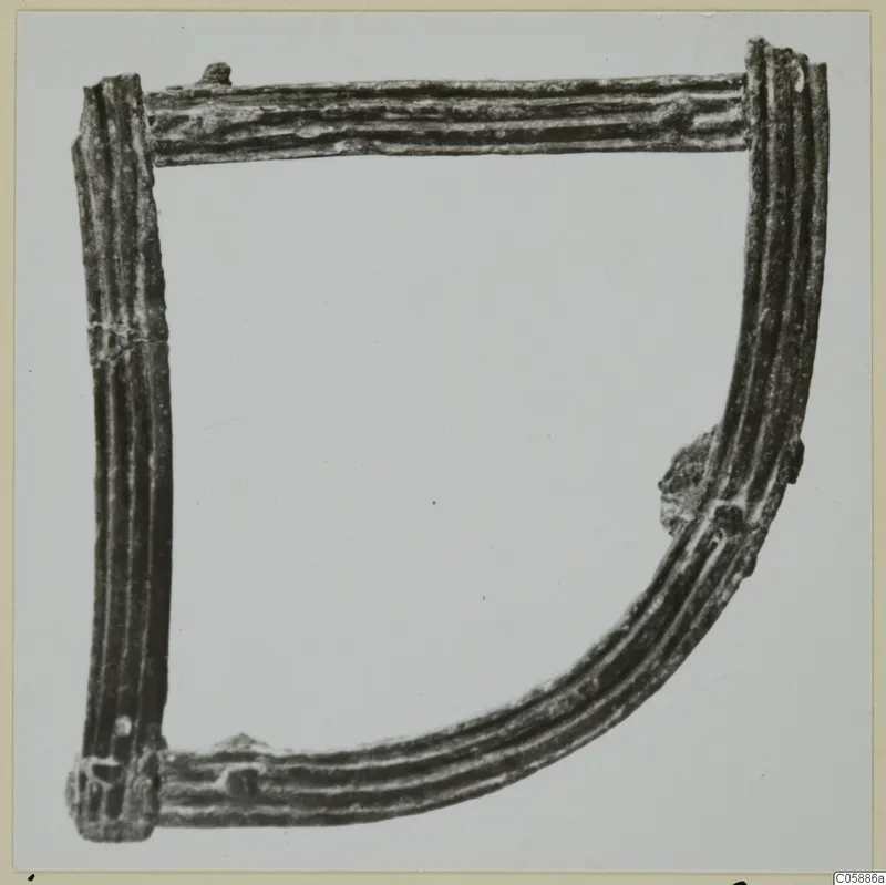 Corroded metal object shaped as an open frame of ribbed bars, with knobs at the corners, shown on a plain light background