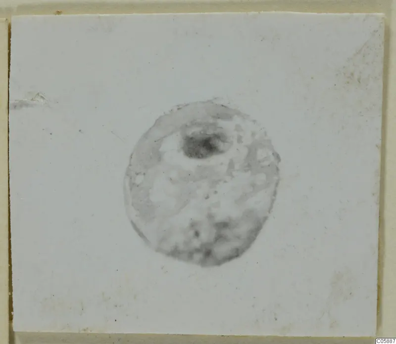 Small round lead bead with a dark hole near the top, photographed on a white card.