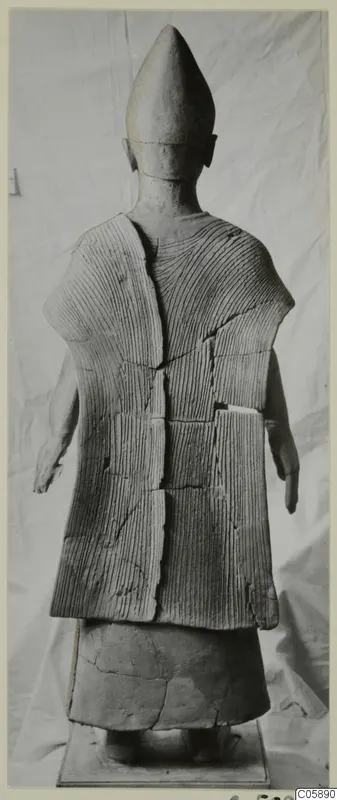 Back view of a terracotta standing figure with a tall conical head and incised parallel lines on its garment