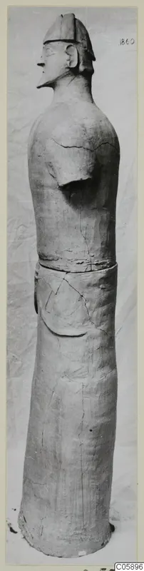 Terracotta standing figure with a helmet-like headdress, shown in profile facing left