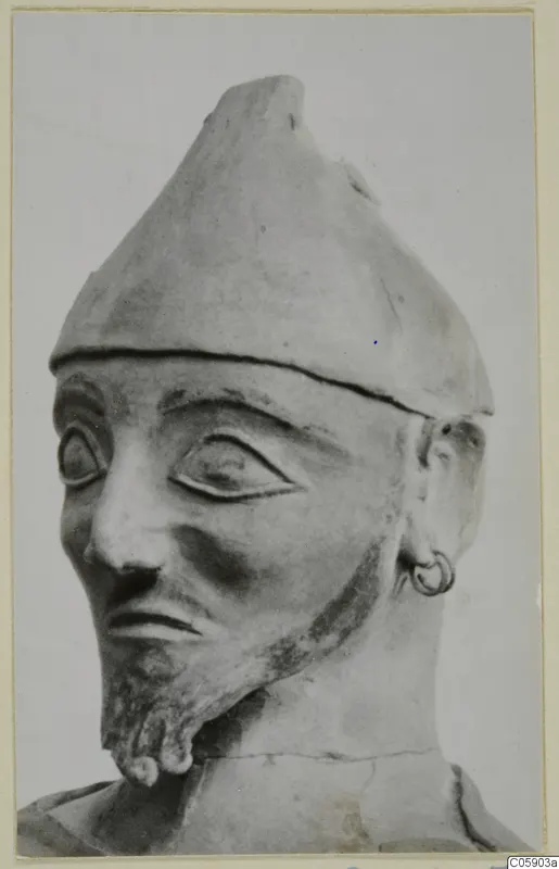 Terracotta head and upper bust of a bearded figure in a conical cap with a ring earring