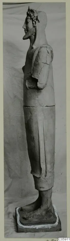 Side view of a tall standing terracotta statue on a square base, with a wreath or headdress and one arm bent at the chest.