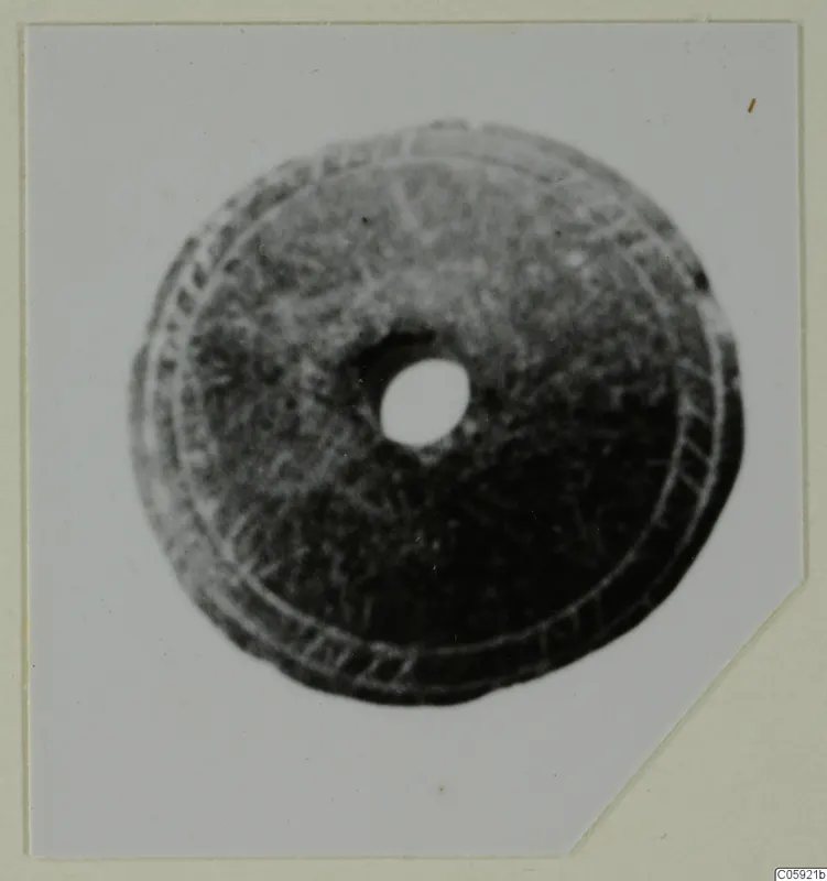 Round disc with a central hole and concentric incised rings, shown in a photograph mounted on a card.