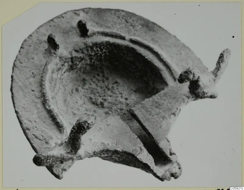 Lamp with a shallow round basin, a long projecting nozzle at right and a curved lug at lower left, seen from above.