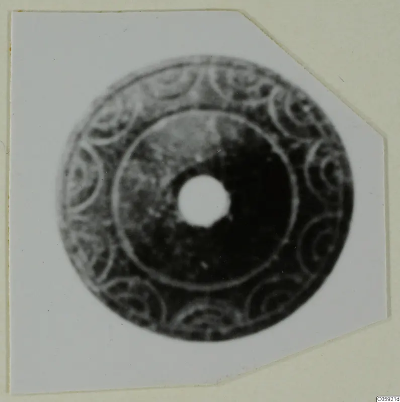 Flat disc-shaped piece of jewellery with a central hole and spiral decoration around its rim
