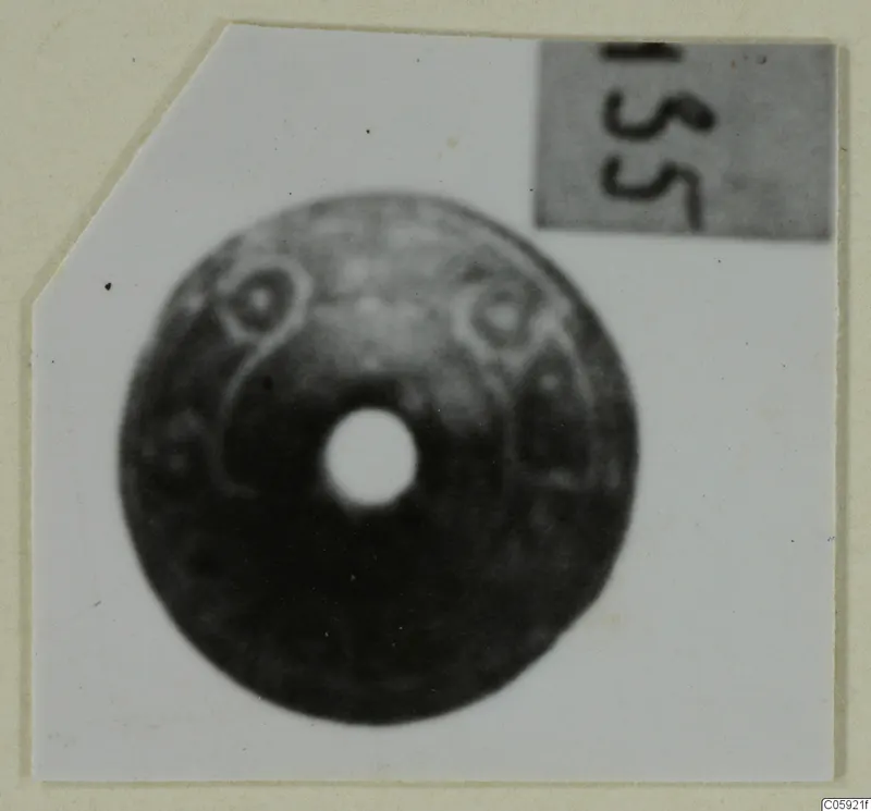Disc-shaped ornament with a large central hole and raised ring motifs, photographed on white card