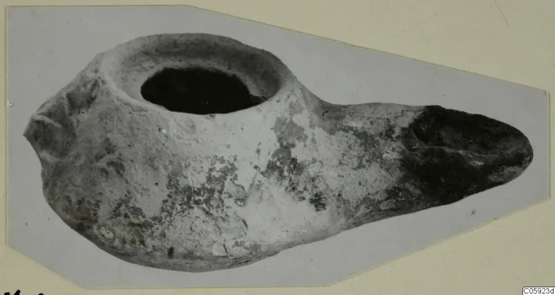 Clay oil lamp with a round filling hole at the top and an elongated nozzle to the right.