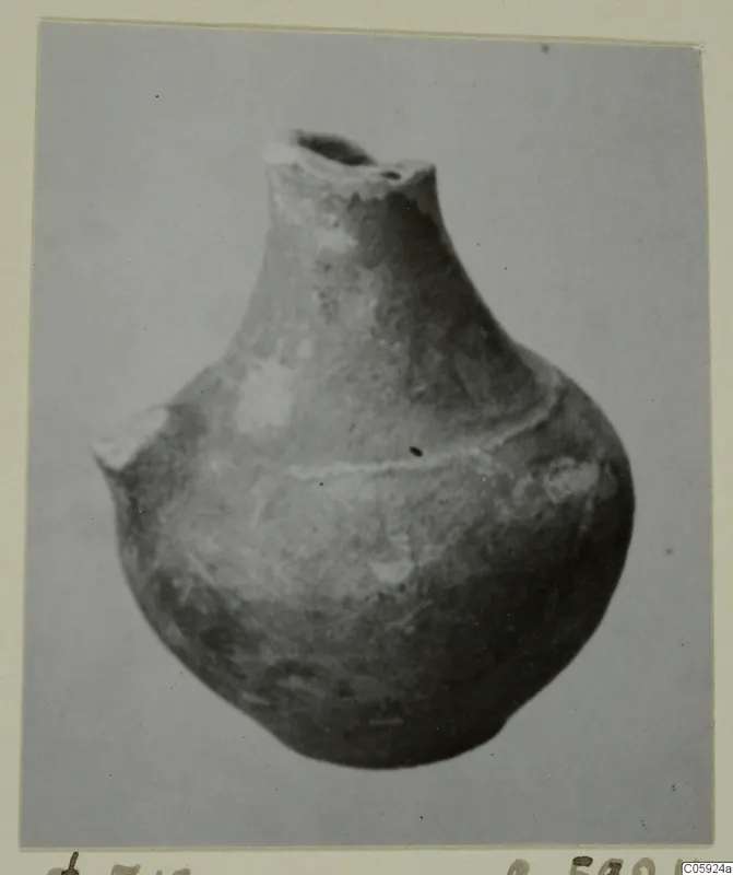 Globular pottery vessel with a short neck and broken rim, photographed against a plain grey background