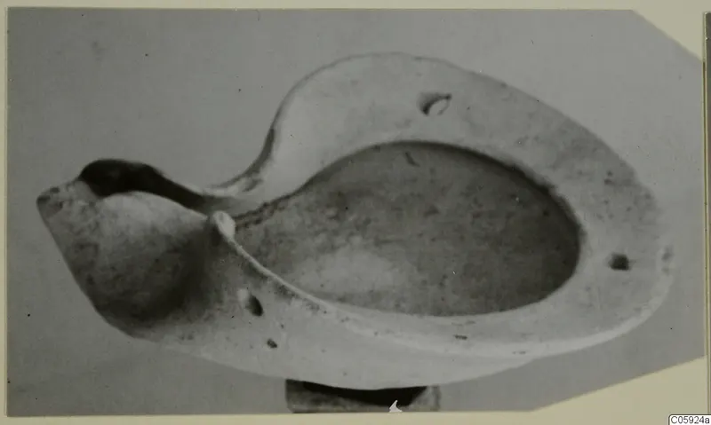 Terracotta lamp with an oval basin, raised rim and pinched spout, photographed against a grey background.