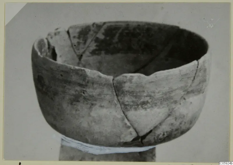 Broken pottery bowl with a wide open mouth and cracks across its walls, photographed against a plain background.