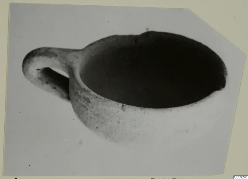 Red slip bowl with a horizontal handle, seen from above at an angle against a plain grey backdrop
