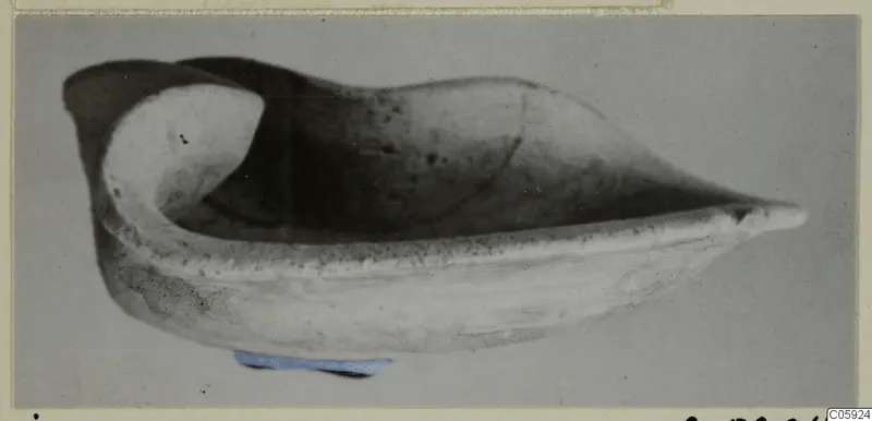 Terracotta lamp with a shallow, boat-shaped body and a pointed nozzle, photographed against a grey backdrop.