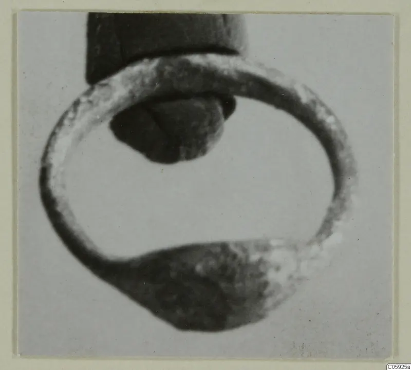 Close-up of a silver ring with a flattened, broader section at the bottom and a dark object inside its loop.