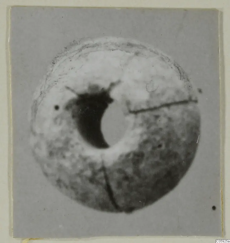 Round bead with a large central hole and cracks across its surface, shown on a grey card