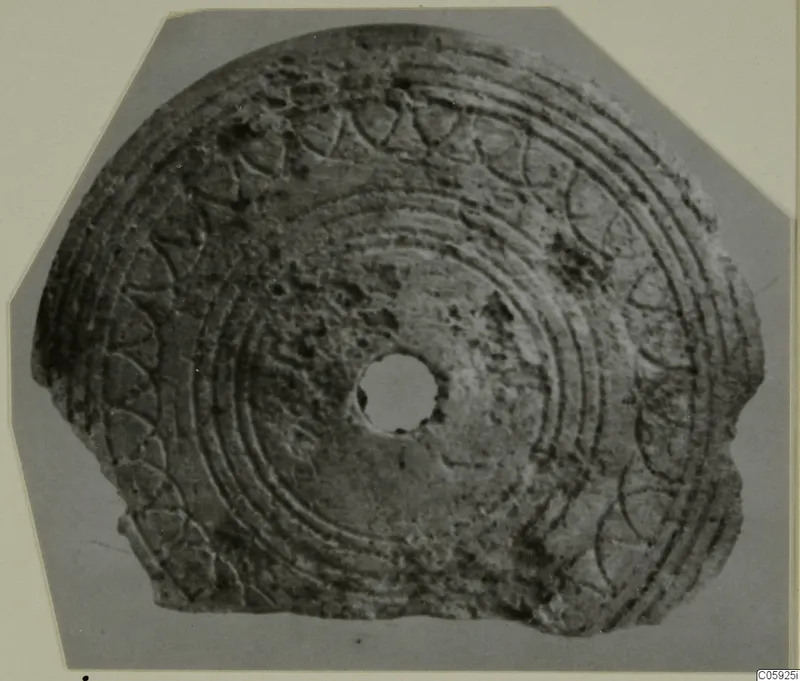 Bone disc with concentric grooves and arc patterns around its edge and a central hole