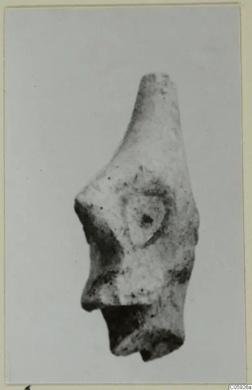 Terracotta figurine fragment with a tapering top, a raised rounded area on the face and a broken base.