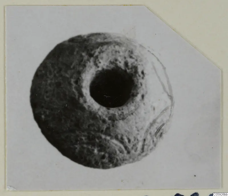 Round object with a large central hole and pitted surface, from Idalion, shown on a mounted card