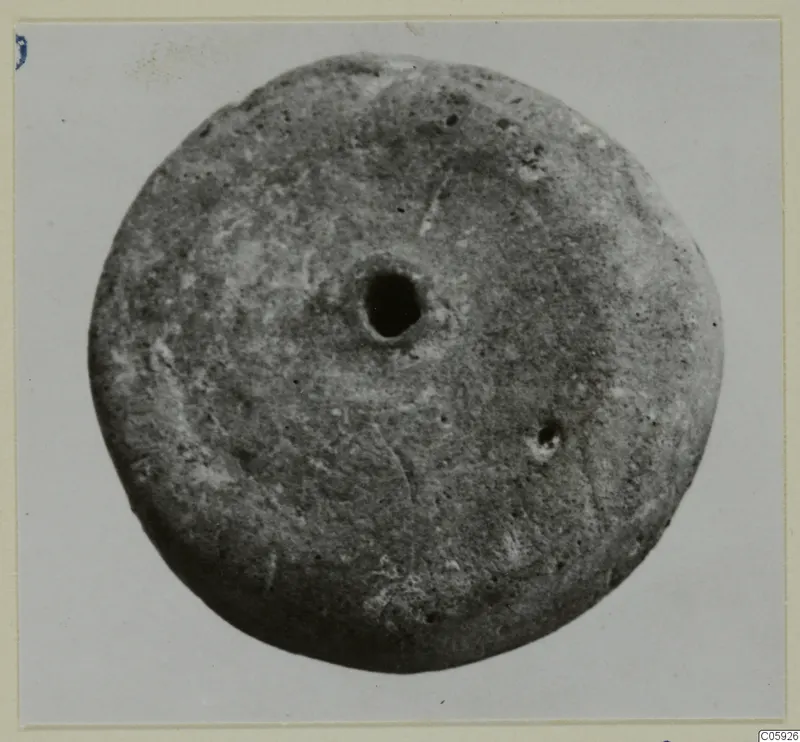 Round disc-shaped small find with a large central hole, photographed against a pale background