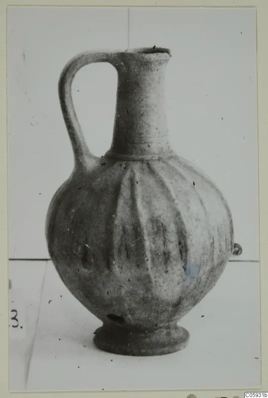 Wheel-made bucchero jug with a single handle, tall neck and vertical ribbing, photographed against a plain background.