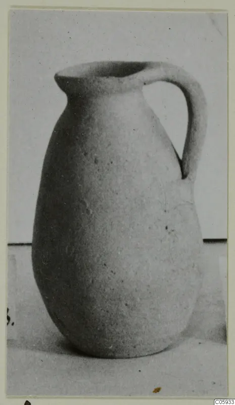 Plain white pottery jug with a single handle, photographed on a pale surface