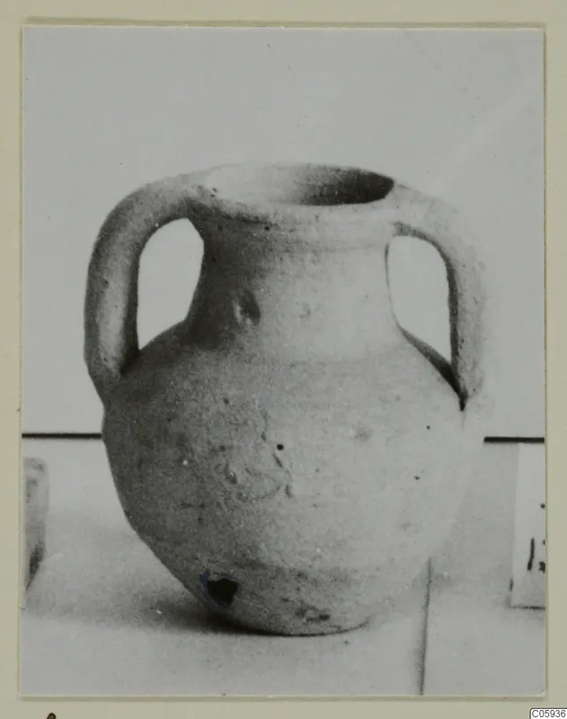 Plain pale pottery jug with two handles and a wide mouth, photographed on a light surface.