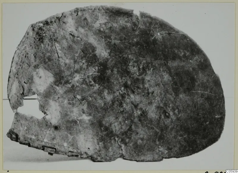 Corroded bronze fragment from Idalion, rounded with broken edges and a hole on the left side