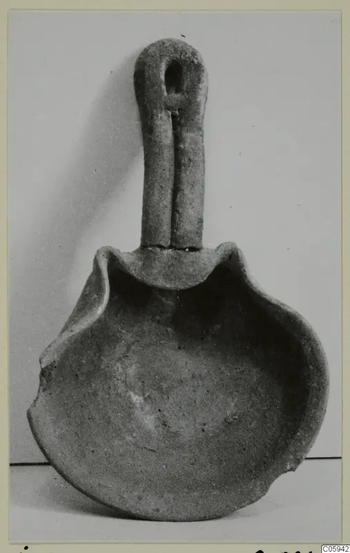 Terracotta lamp with a tall loop handle and a shallow open bowl with a pinched rim.