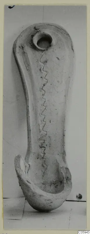 Pottery object from Idalion with a round hole at one end, a wavy incised line down its length and a curved, broken lower end